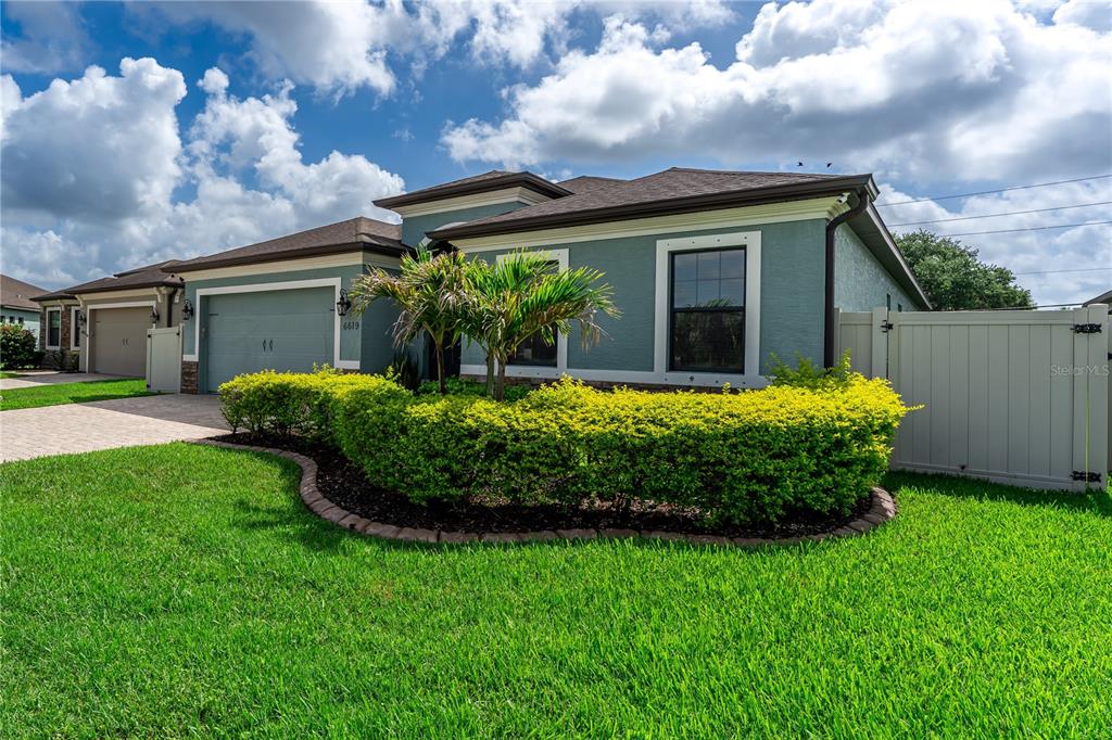 A teal single-story house features a two-car garage, a manicured hedge, and a vinyl fence — 6619 35TH COURT E, SARASOTA, FL