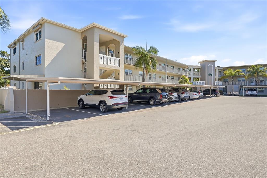 A three-story apartment building with a covered parking area and several parked cars — 952 VIRGINIA STREET UNIT 202, DUNEDIN, FL