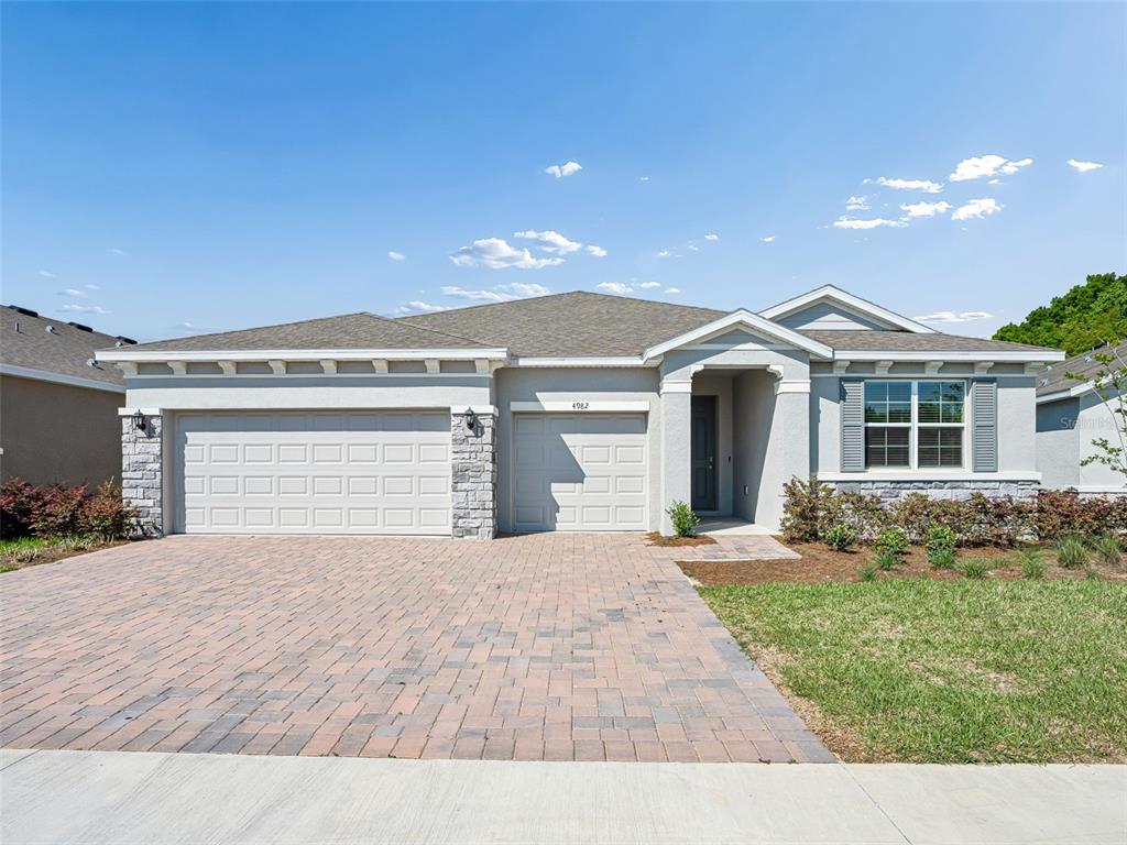 A single-story house features a stone-accented facade, a paver driveway, and a three-car garage — 4982 NW 39TH LOOP, OCALA, FL