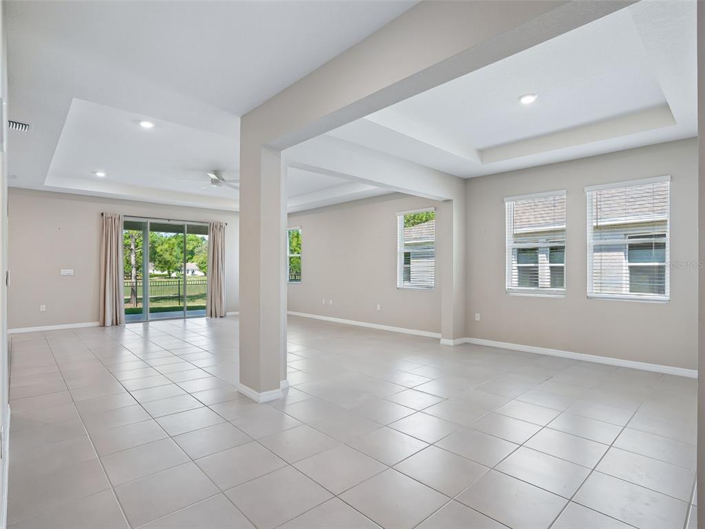 An empty living area features light-colored tile flooring, recessed tray ceilings, and large windows — 4982 NW 39TH LOOP, OCALA, FL