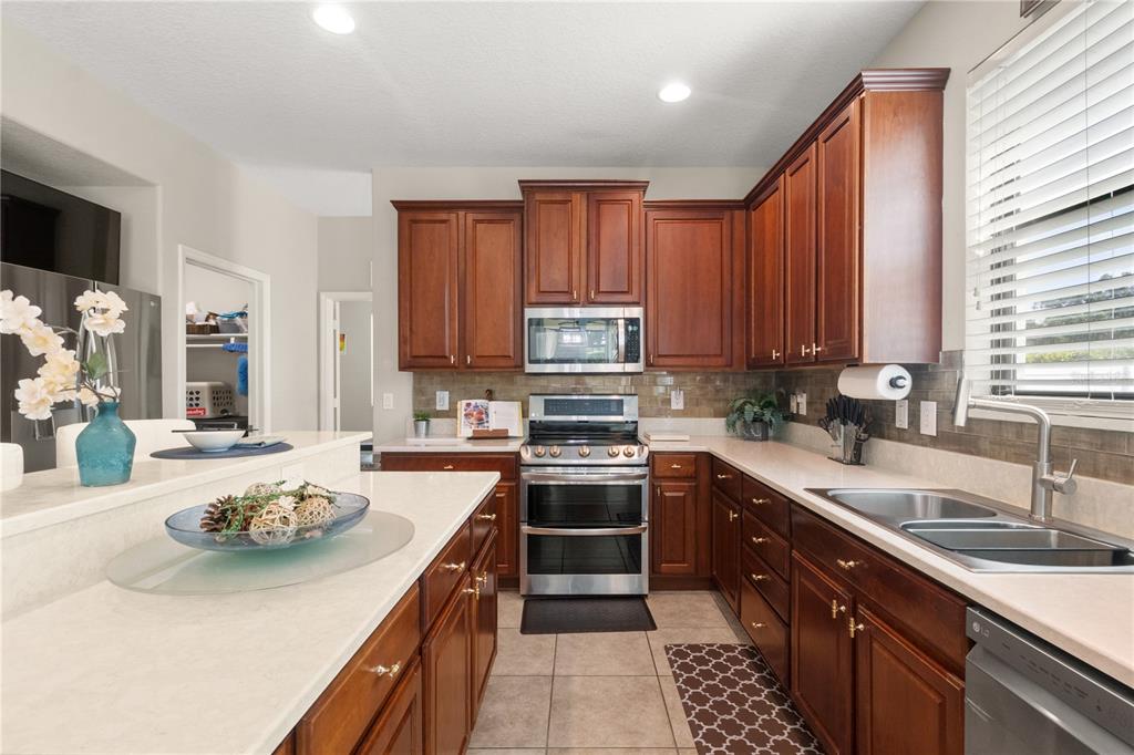 A kitchen features wood cabinets, stainless steel appliances, and a white countertop island — 5824 FISH CROW PLACE, LAND O LAKES, FL