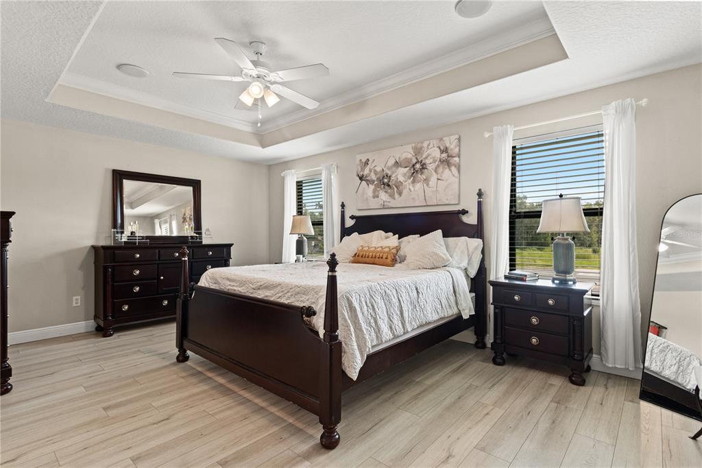 A bedroom features a dark wood bed frame, matching furniture, and light wood-look flooring — 5824 FISH CROW PLACE, LAND O LAKES, FL