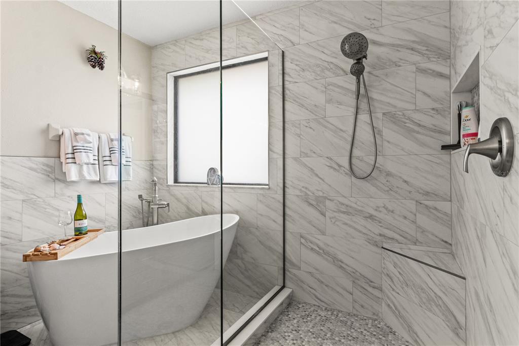 A modern bathroom features a freestanding soaking tub and a walk-in shower with marble-look tiles — 5824 FISH CROW PLACE, LAND O LAKES, FL