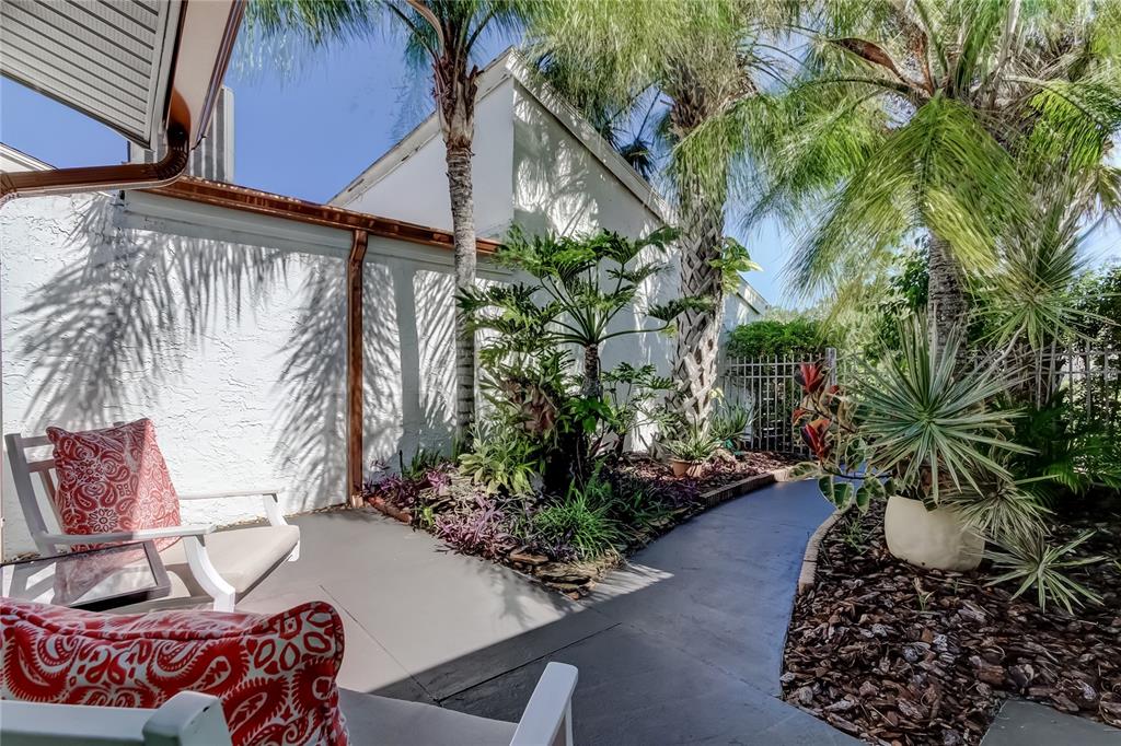 A patio with white chairs, tropical plants, and a curved walkway beside a white wall — 12625 SHELL POINT DRIVE, HUDSON, FL