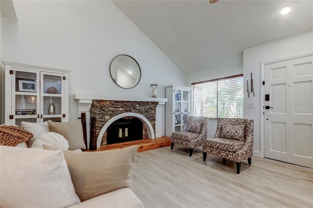 A living room features a stone fireplace, vaulted ceilings, light wood flooring, and two armchairs — 12625 SHELL POINT DRIVE, HUDSON, FL