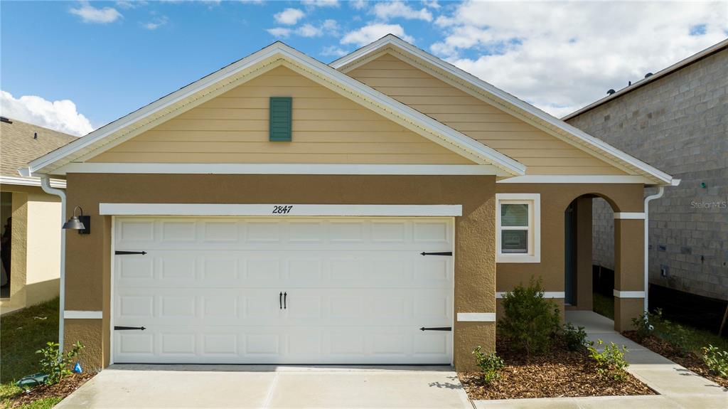 The exterior of a one-story house features a two-car garage and a covered entryway — 2847 COMMON CRANE COURT, HARMONY, FL