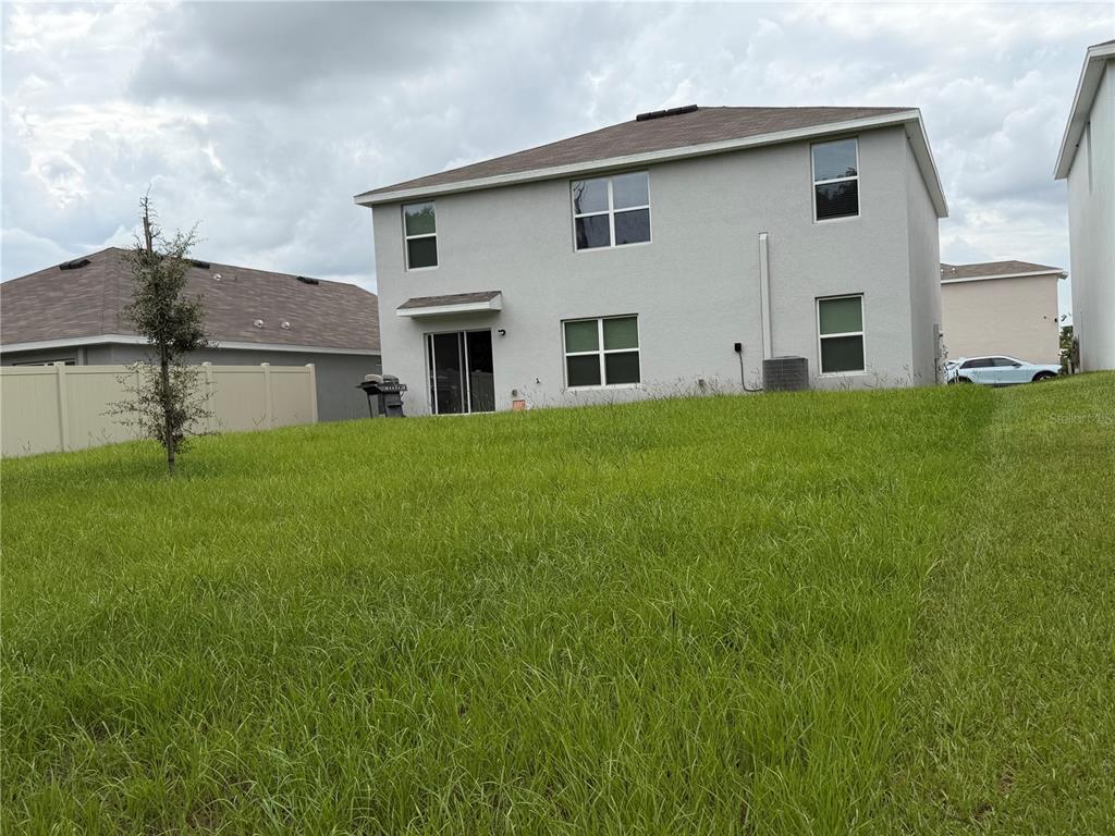The rear exterior of a two-story house features a grassy yard and a sliding door — 7737 ROSEWOOD GARDEN LOOP, TAMPA, FL