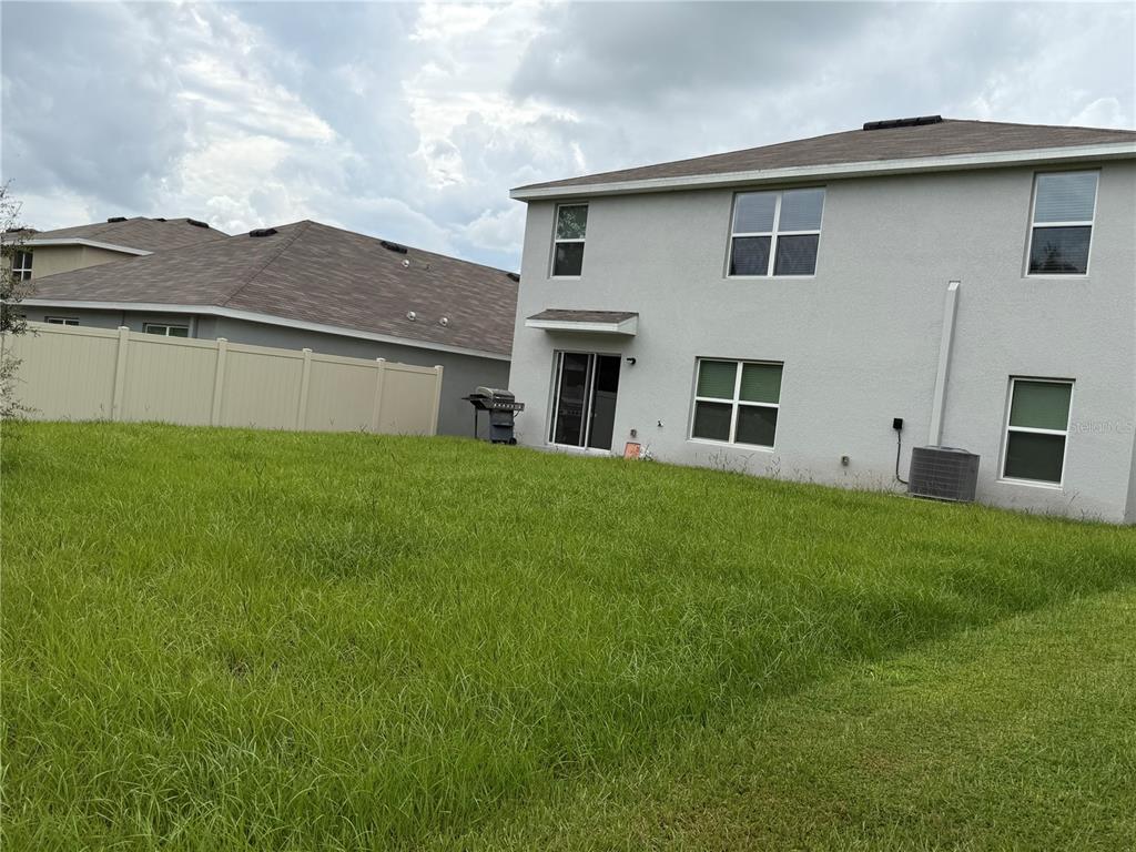 The backyard of a two-story house features a tan vinyl fence and a central lawn — 7737 ROSEWOOD GARDEN LOOP, TAMPA, FL