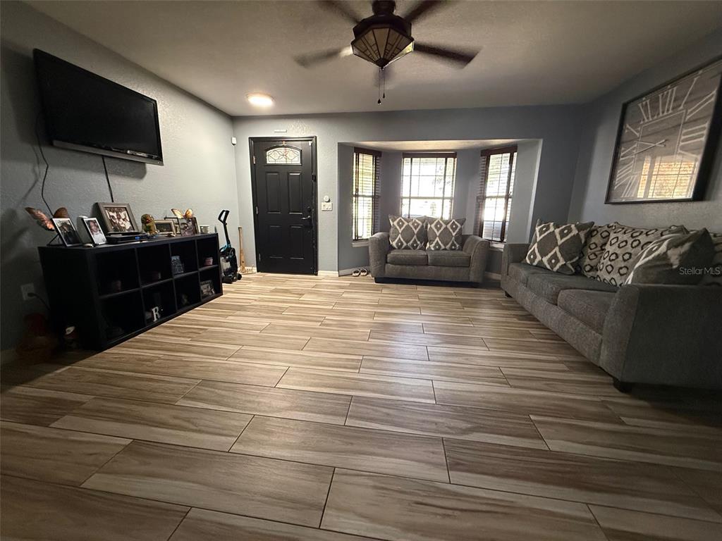 A living room features wood-look tile flooring, a black front door, and two grey sofas — 710 BLUEBILL PLACE, KISSIMMEE, FL