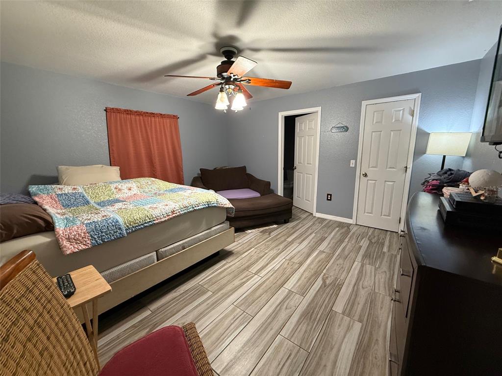 A bedroom features a bed with a colorful quilt, wood-look tile flooring, and a ceiling fan — 710 BLUEBILL PLACE, KISSIMMEE, FL