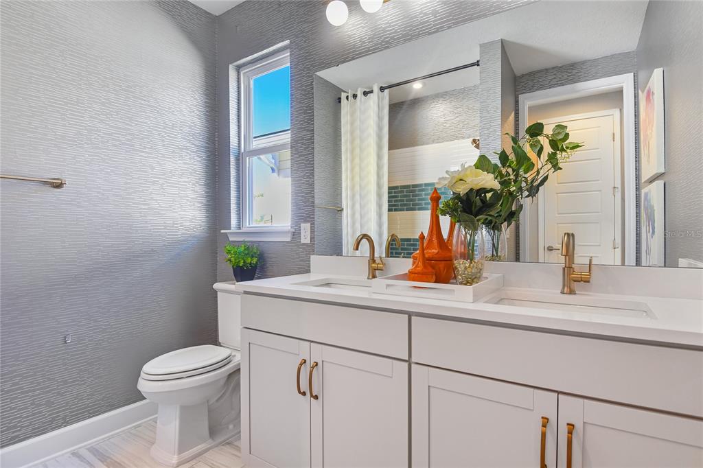 A bathroom features a double vanity with gold fixtures, gray textured wallpaper, and a window — 204 THORNBERRY WAY, PALM COAST, FL