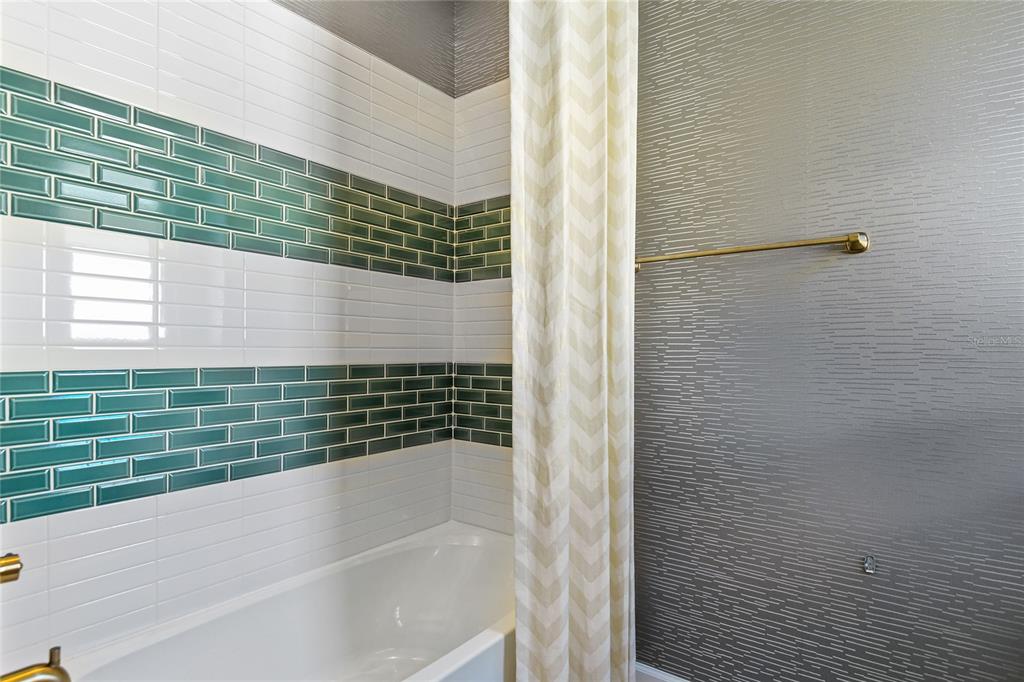 A bathroom features a white bathtub, green and white subway tile, and textured gray wallpaper — 204 THORNBERRY WAY, PALM COAST, FL