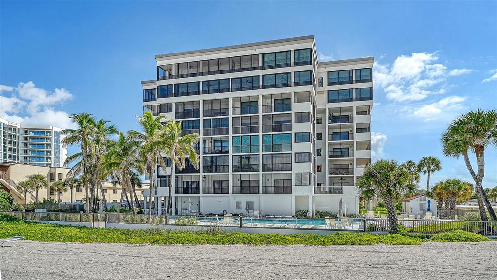 A multi-story beachfront condominium building features screened balconies and a ground-level swimming pool — 1100 BENJAMIN FRANKLIN DRIVE UNIT 204, SARASOTA, FL