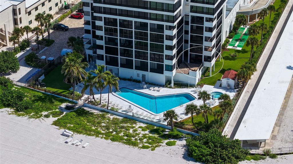 An aerial view shows a high-rise building with a pool, palm trees, and beach access — 1100 BENJAMIN FRANKLIN DRIVE UNIT 204, SARASOTA, FL