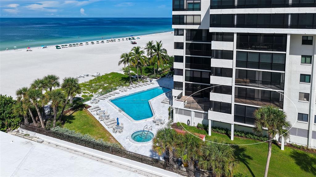 An aerial view shows a beachfront condominium building with a pool, patio, and palm trees — 1100 BENJAMIN FRANKLIN DRIVE UNIT 204, SARASOTA, FL