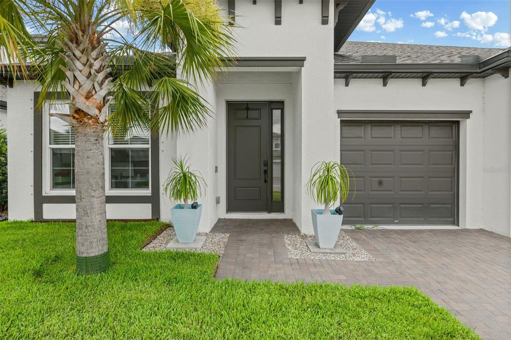 A white house exterior features a dark front door, a garage, and a palm tree — 1024 FERNLEAF RUN, BRADENTON, FL