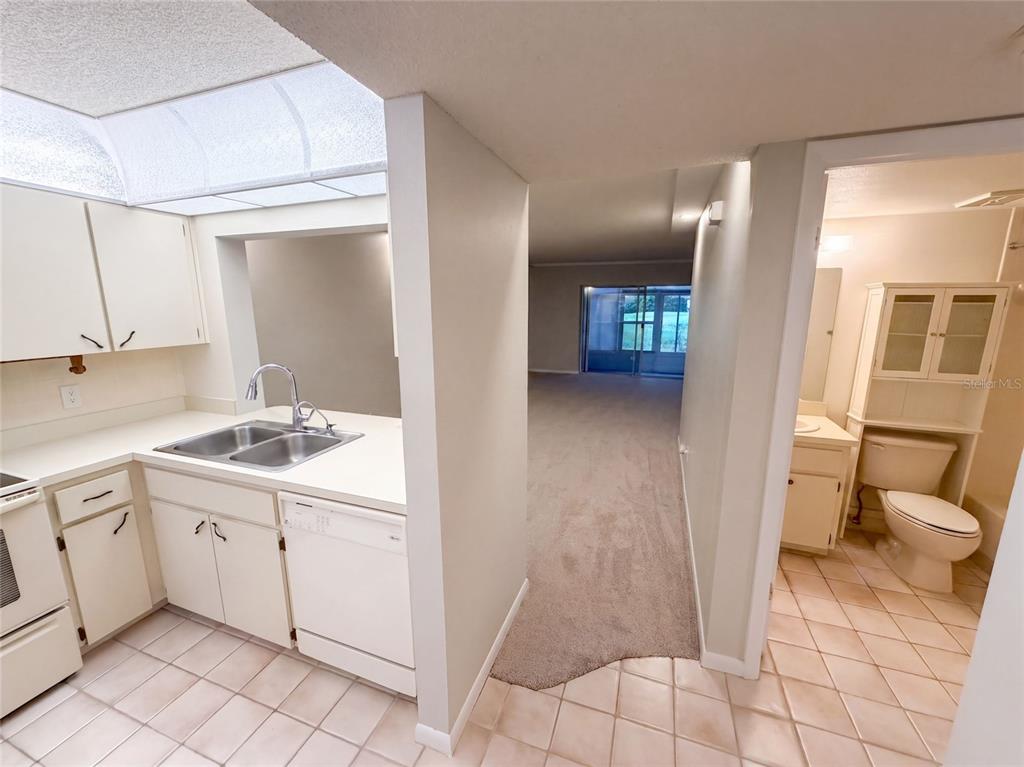 A kitchen with white cabinets and a double sink opens to a carpeted living area — 1465 MILLSTREAM LANE UNIT 104, DUNEDIN, FL