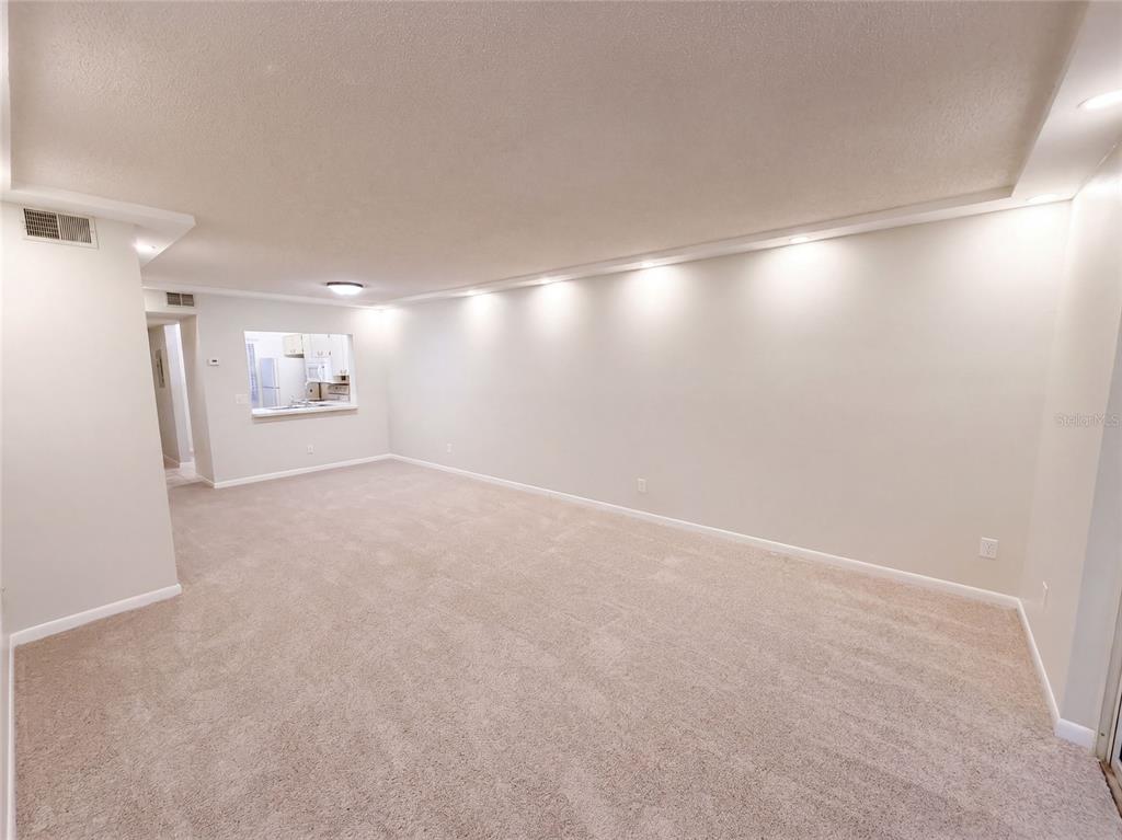 An empty living room features beige carpeting, neutral walls, and recessed lighting along the ceiling — 1465 MILLSTREAM LANE UNIT 104, DUNEDIN, FL
