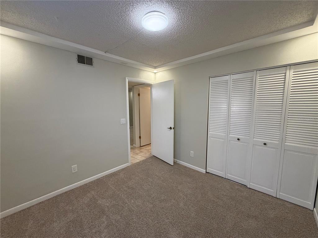 A bedroom with beige carpet, light gray walls, a white door, and white louvered closet doors — 1465 MILLSTREAM LANE UNIT 104, DUNEDIN, FL