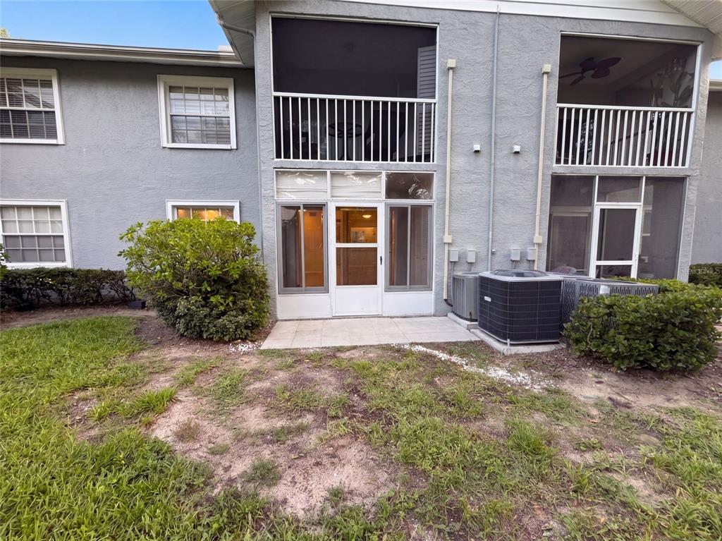 A two-story building exterior features screened-in balconies, a ground-level patio, and an air conditioning unit — 1465 MILLSTREAM LANE UNIT 104, DUNEDIN, FL