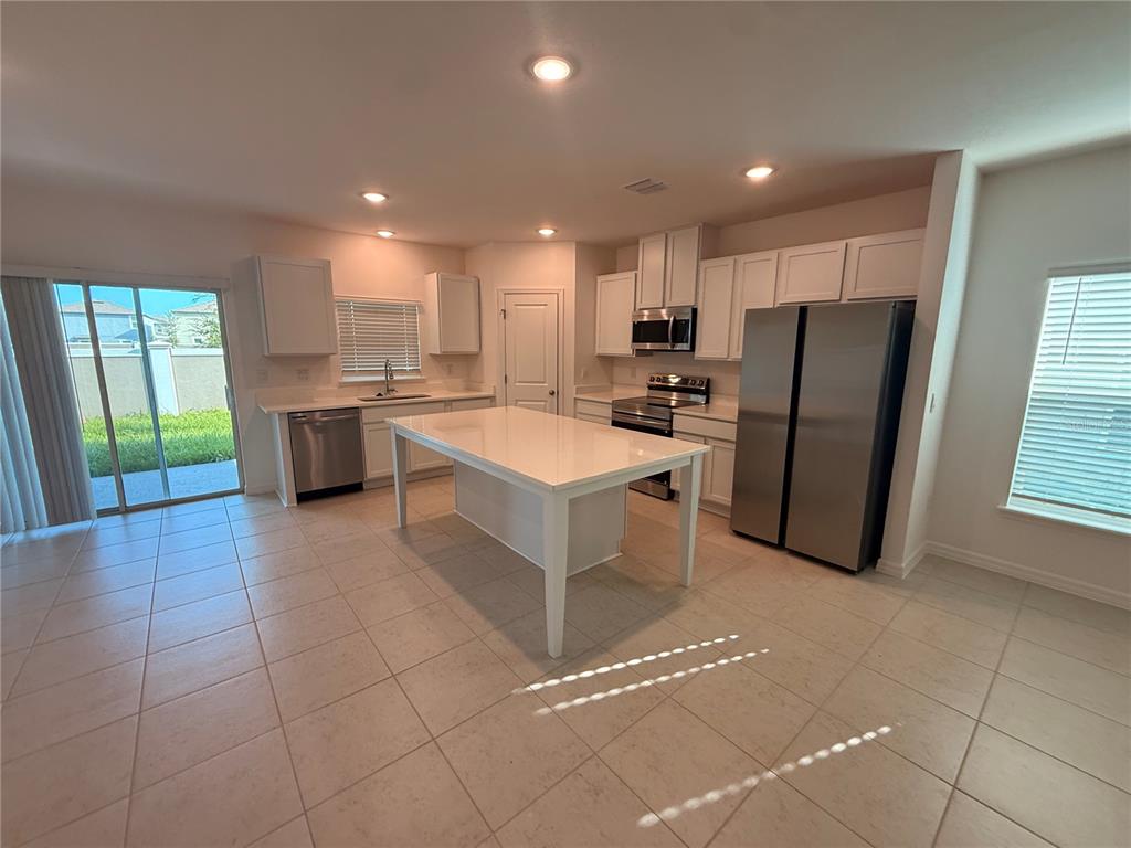 A kitchen features white cabinets, stainless steel appliances, a central island, and tiled flooring — 10771 IRONWOOD TREE WAY, SAN ANTONIO, FL