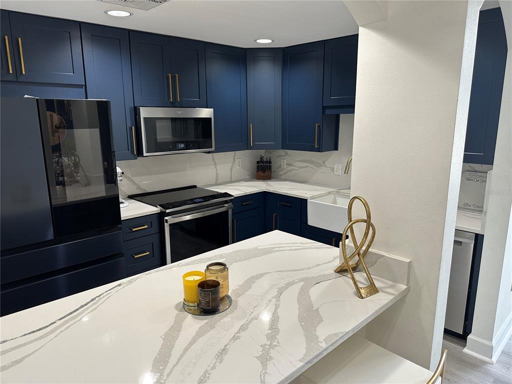 A kitchen features dark blue cabinets, white marble-patterned countertops, and stainless steel appliances — 808 3RD AVENUE W UNIT 701, BRADENTON, FL