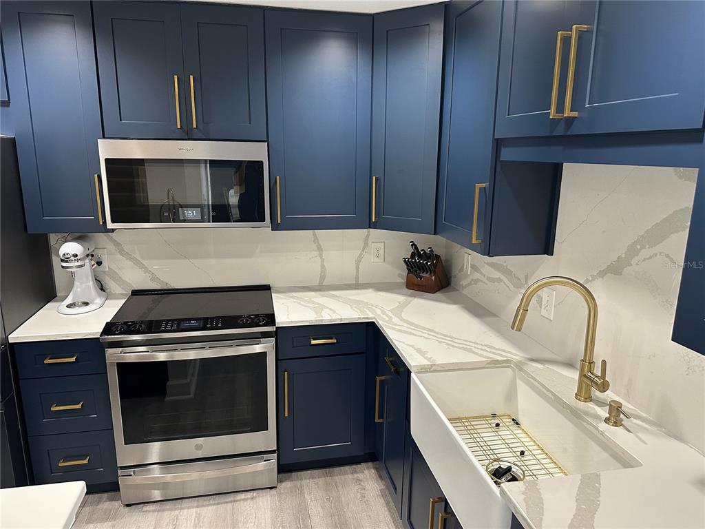 A kitchen features dark blue cabinets, gold hardware, a farmhouse sink, and white marble countertops — 808 3RD AVENUE W UNIT 701, BRADENTON, FL