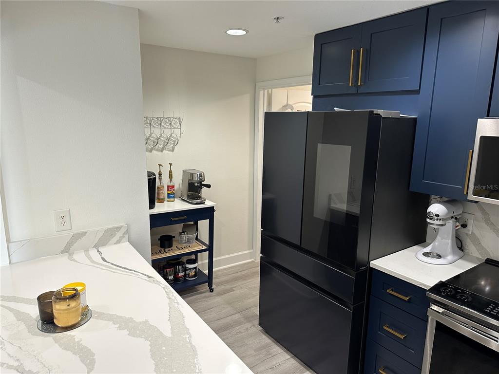 A kitchen features dark blue cabinets, a black refrigerator, and a small coffee bar cart — 808 3RD AVENUE W UNIT 701, BRADENTON, FL