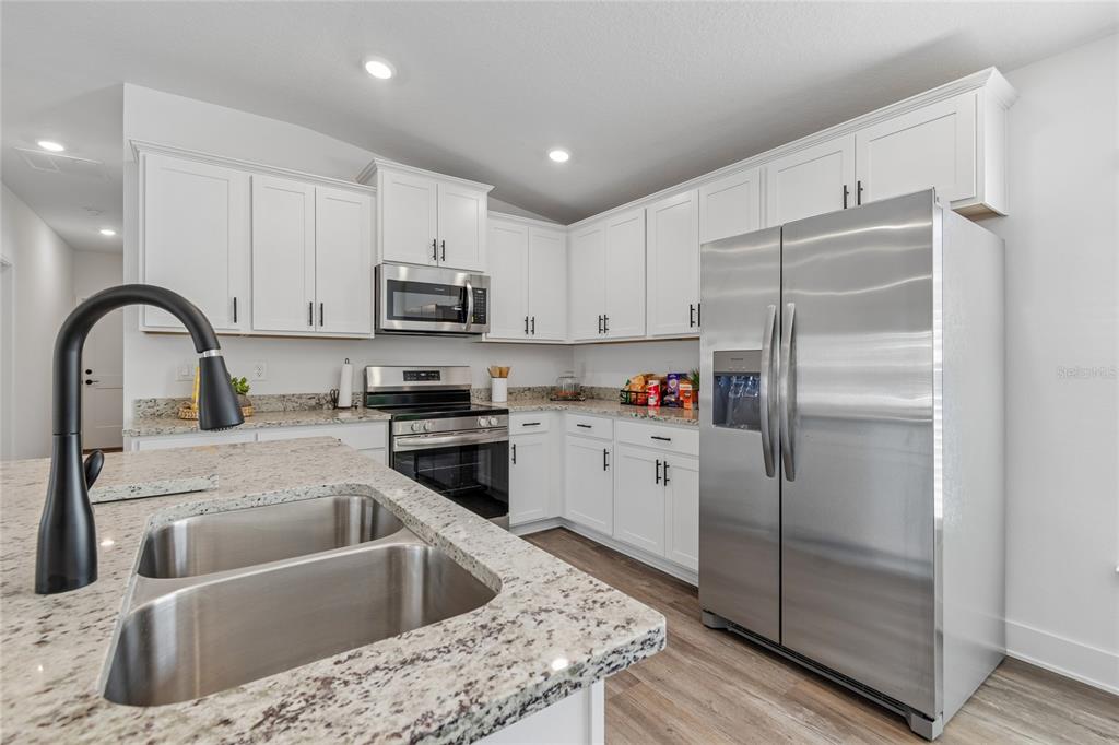 A kitchen with white cabinets, granite countertops, stainless steel appliances, and a large island sink — 9409 HIGHLAND HILLS DR STREET, HUDSON, FL