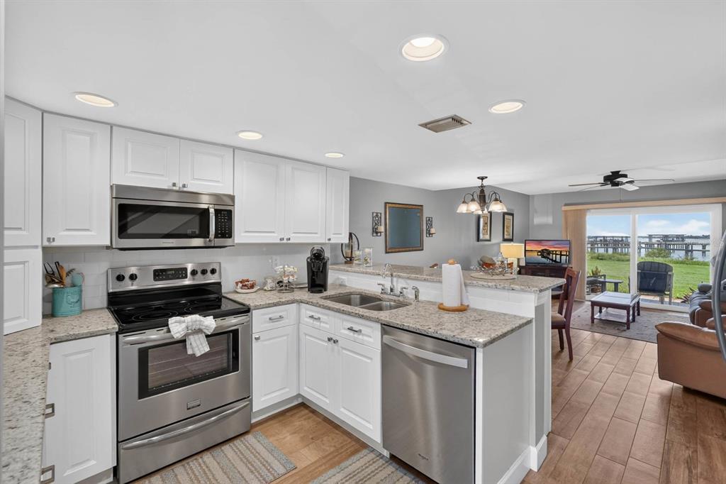 A kitchen with white cabinets, stainless steel appliances, and granite countertops overlooks a living area — 7265 A1A S UNIT B8, ST AUGUSTINE BEACH, FL