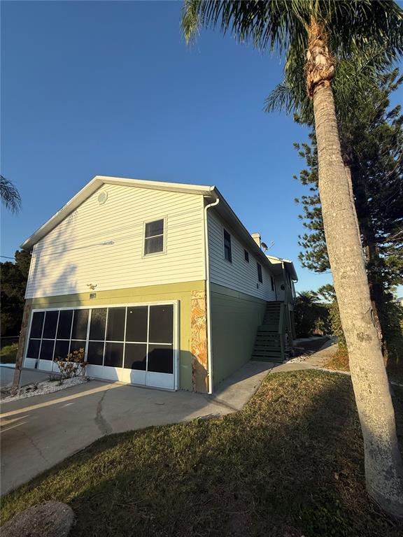An elevated house with light-colored siding, a screened-in lower level, and a palm tree nearby — 3338 FERNLEAF DRIVE, HERNANDO BEACH, FL
