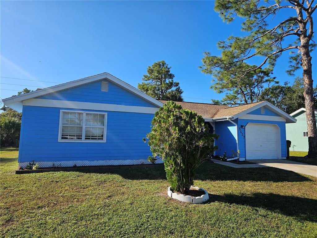 A blue single-story house with a white garage door and a front yard tree — 5437 TALBROOK ROAD, NORTH PORT, FL