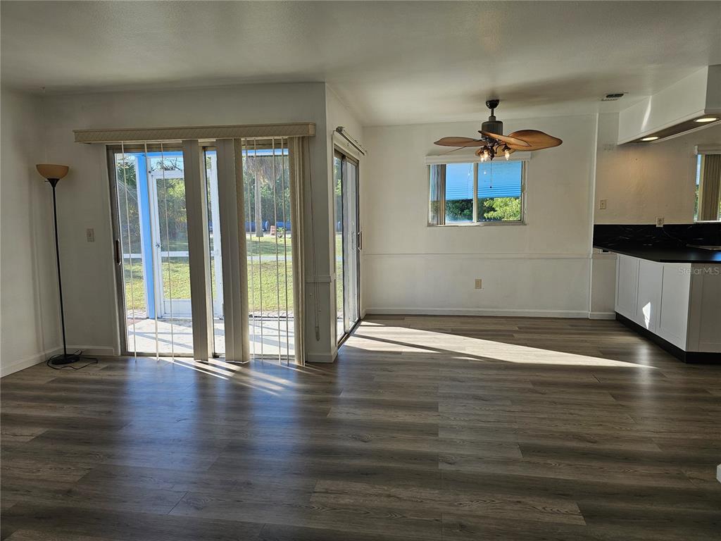 A living area with wood-look flooring, sliding glass doors, a ceiling fan, and kitchen access — 5437 TALBROOK ROAD, NORTH PORT, FL