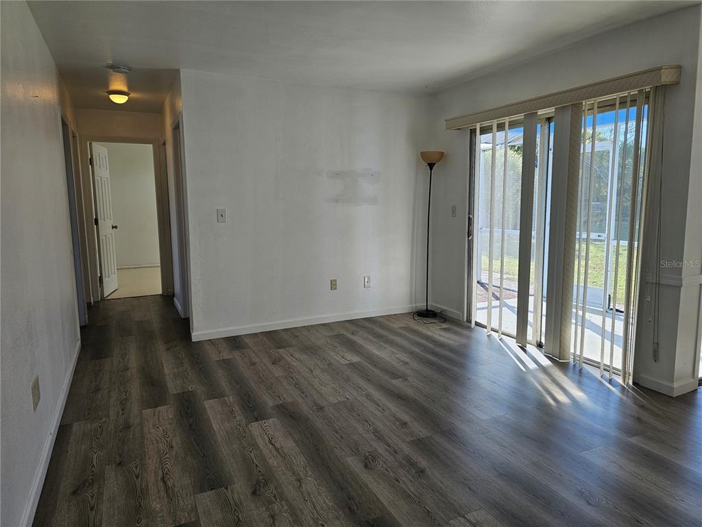 An empty room features wood-look flooring, white walls, and a sliding glass door to a patio — 5437 TALBROOK ROAD, NORTH PORT, FL
