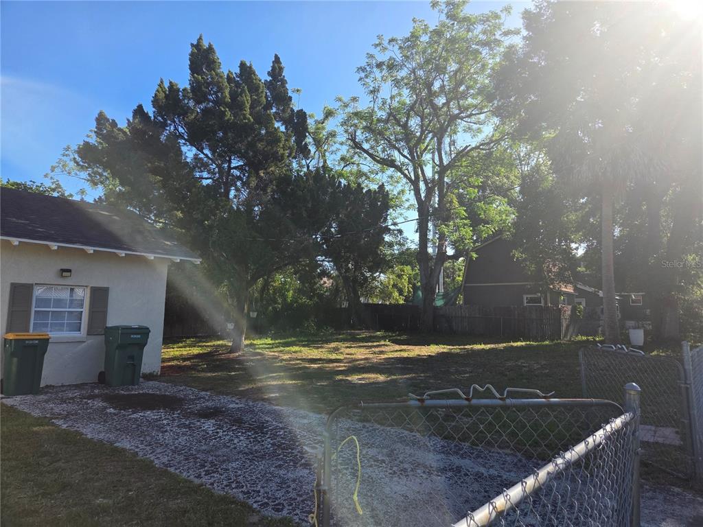 A grassy backyard features mature trees, a gravel driveway, and a chain-link fence — 101 E ATWATER AVENUE, EUSTIS, FL