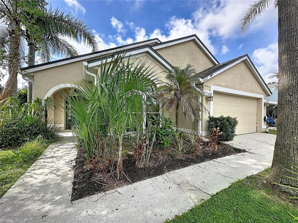 A single-story house with a beige stucco exterior, a two-car garage, and a landscaped front yard — 1047 KELLY CREEK CIRCLE, OVIEDO, FL