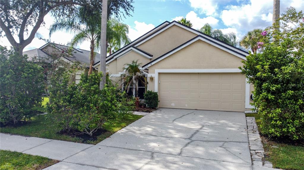 A tan single-story house features a two-car garage, a concrete driveway, and surrounding landscaping — 1047 KELLY CREEK CIRCLE, OVIEDO, FL