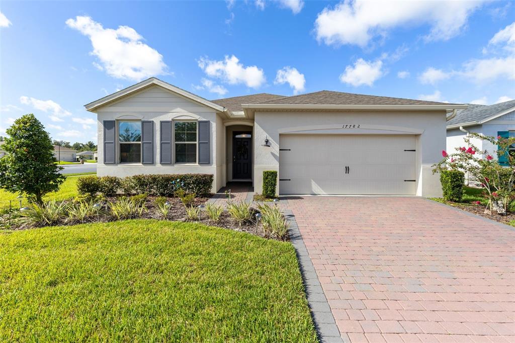 A single-story house with a beige exterior, a brick paver driveway, and a two-car garage — 17782 BLAZING STAR CIRCLE, CLERMONT, FL