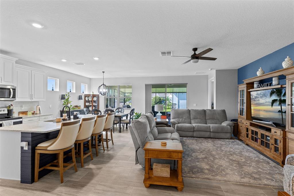 An open-concept living room and kitchen featuring a large island, gray sofa, and wood entertainment center — 17782 BLAZING STAR CIRCLE, CLERMONT, FL