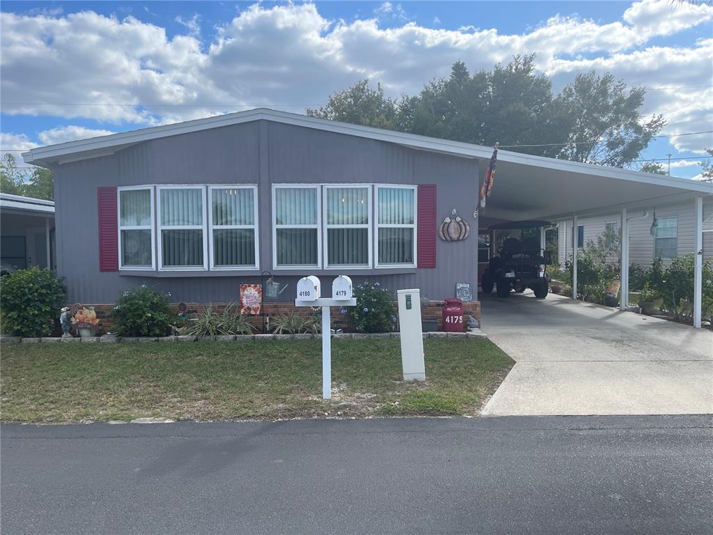A gray single-story manufactured home features a carport, a front lawn, and two mailboxes — 4179 ROLLING OAKS DRIVE, WINTER HAVEN, FL