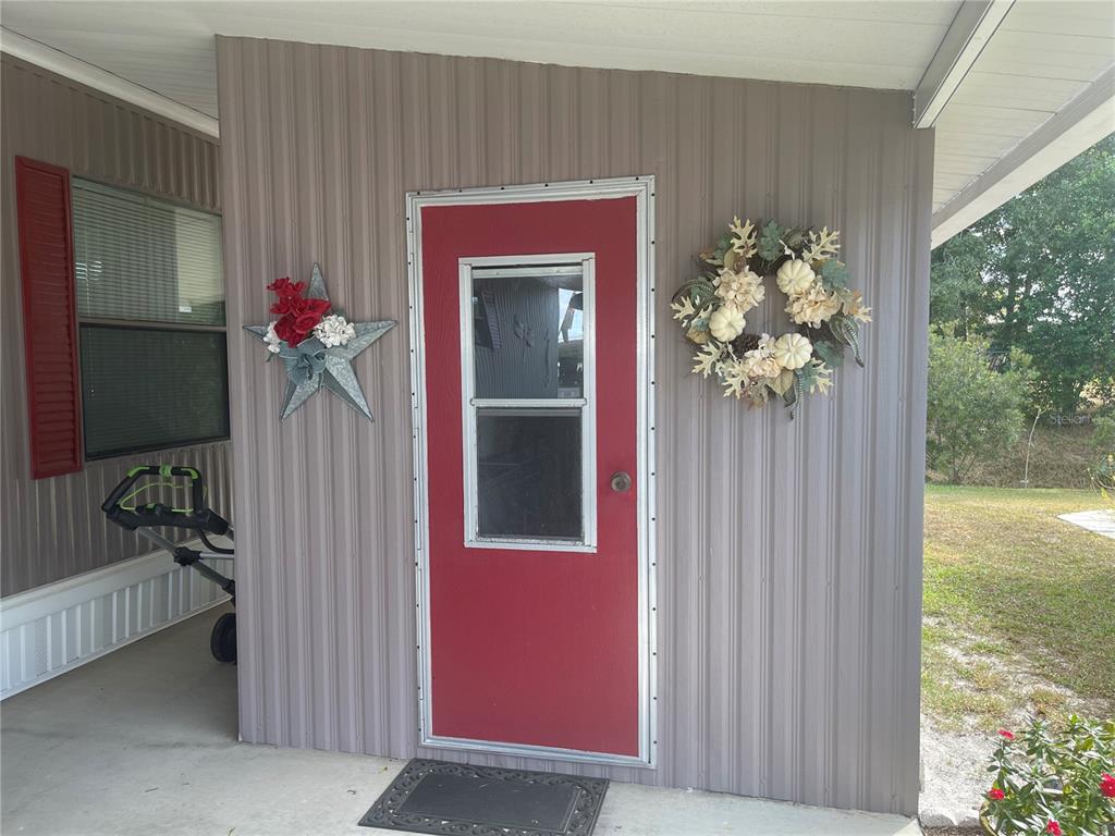 A red door with a window is centered on a tan metal-sided exterior wall — 4179 ROLLING OAKS DRIVE, WINTER HAVEN, FL