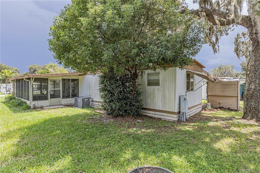 A mobile home exterior with a screened-in porch, metal siding, and a large shade tree — 5160 S FLORENCE TERRACE, FLORAL CITY, FL