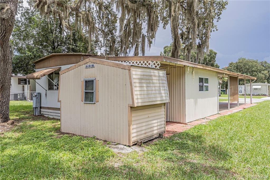 A mobile home exterior features a beige storage shed and a covered carport area — 5160 S FLORENCE TERRACE, FLORAL CITY, FL
