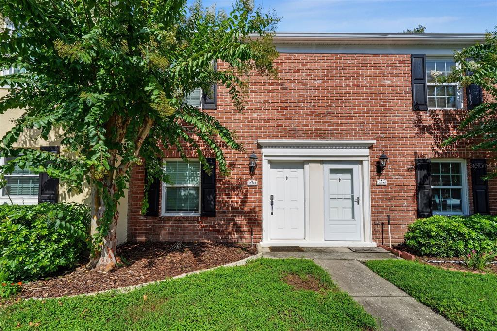 A two-story brick townhouse exterior features two white front doors and a small front lawn — 13747 JUNIPER BLOSSOM DRIVE, TAMPA, FL