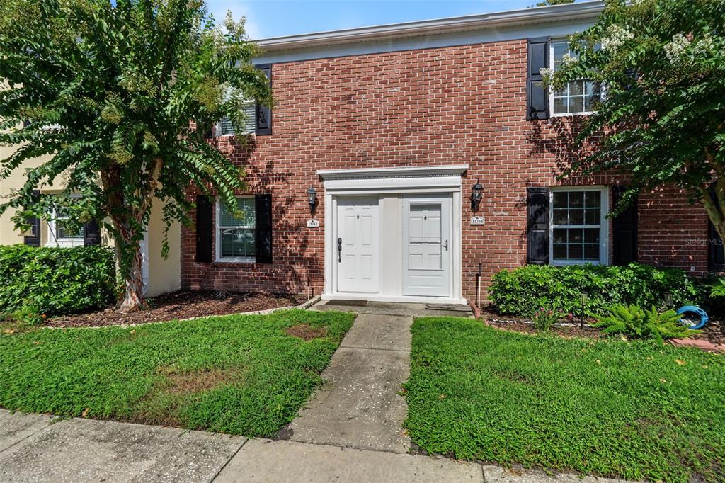 A two-story brick townhouse with two white front doors and green landscaping — 13747 JUNIPER BLOSSOM DRIVE, TAMPA, FL