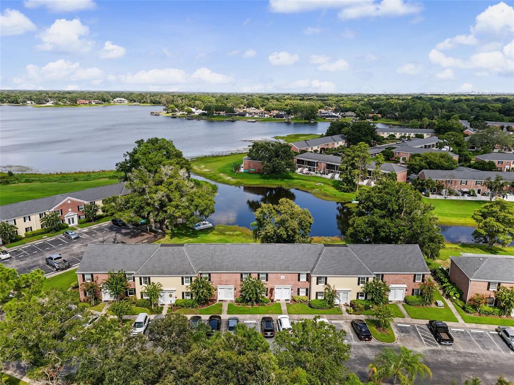 An aerial view shows a multi-unit residential building with a parking lot and nearby lake — 13747 JUNIPER BLOSSOM DRIVE, TAMPA, FL