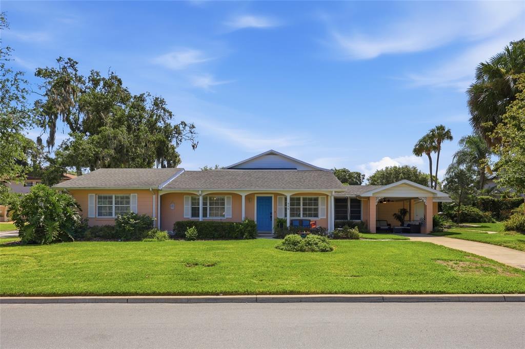 A single-story peach-colored house with a blue front door and an attached carport — 936 N BAKER STREET, MOUNT DORA, FL