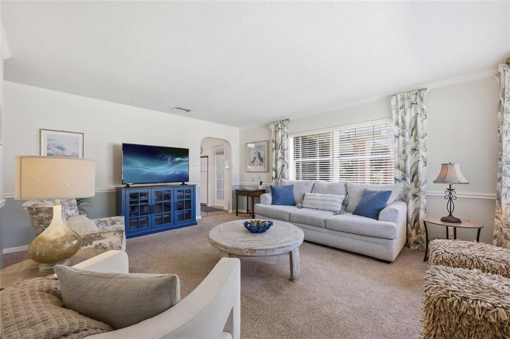 A living room features a grey sofa, blue media console, round coffee table, and carpeted floors — 936 N BAKER STREET, MOUNT DORA, FL