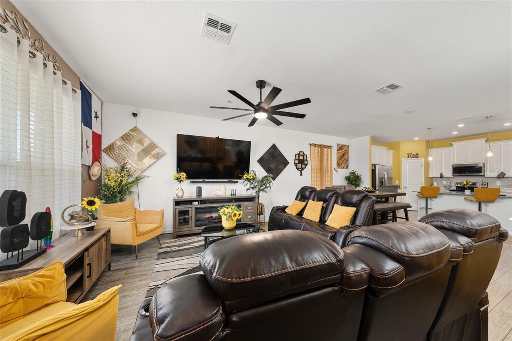 A living room with dark leather recliners, a television, and an open kitchen in the background — 2369 VOLUNTEER AVENUE, KISSIMMEE, FL