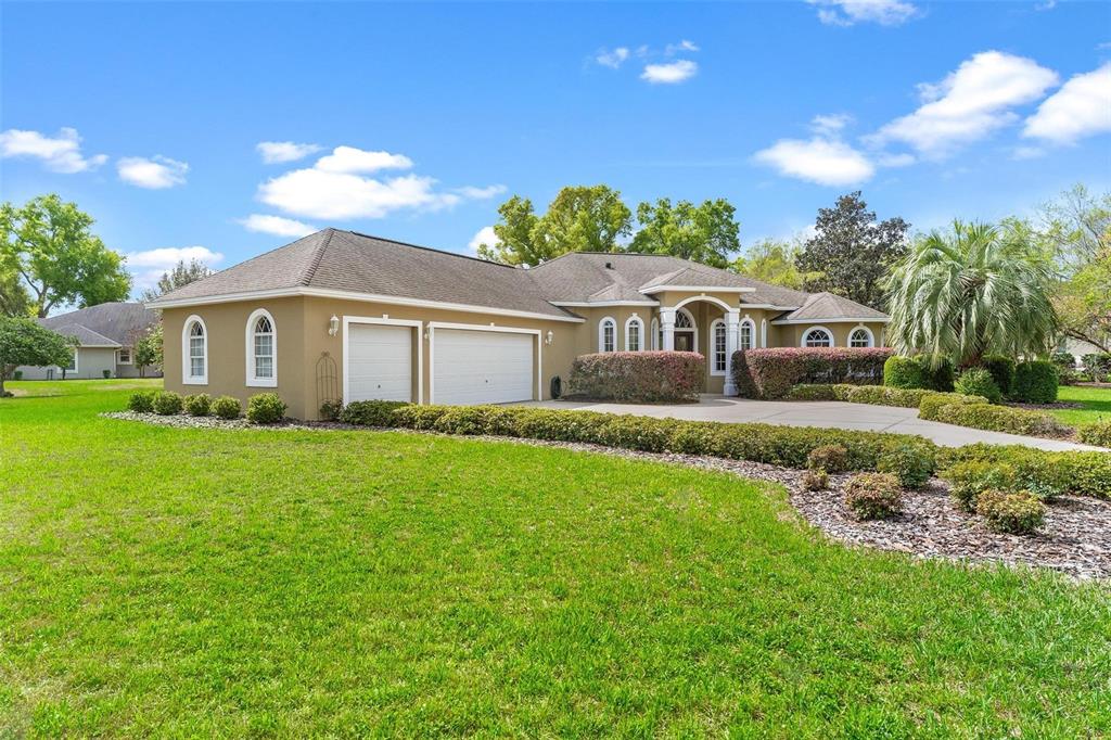 A tan single-story house with a two-car garage and a landscaped front yard — 6053 SPINNAKER LOOP, LADY LAKE, FL